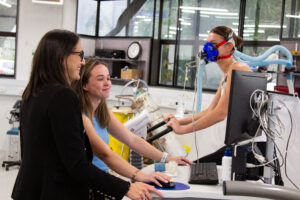 Olivia in the lab with student and person on treadmill wearing a mask to monitor breathing